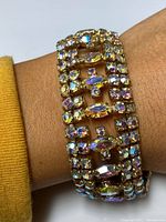 Bracelet worn on wrist displaying iridescent rhinestone embellishments on gold-tone metal base.