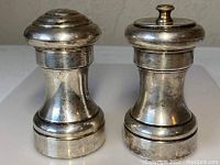 Pair of vintage silver salt and pepper grinders shown side by side on white background.