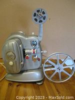 Full view of the silver Noris 8mm film projector with film reel attached and additional reel beside it.