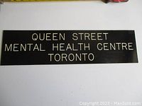 Front view of black sign displaying text ‘QUEEN STREET MENTAL HEALTH CENTRE TORONTO’