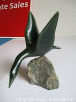 Front side view of the dark green jade flying goose sculpture mounted on rough jade base showing bird's neck stretched forward and wings upright.