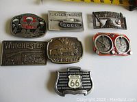 Top-down photo of seven USA themed metal belt buckles arranged in two rows on white background