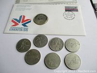 Photo showing the Commonwealth Games first day cover with a visible 50% silver dollar coin and seven Olympics coins.