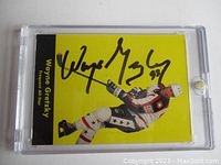 Front view of Wayne Gretzky hockey card with black signature on yellow background inside magnetic plastic holder.