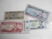 Four Iraqi dinar bills including 1, 5, 50, and 100 denominations in protective sleeves, showing fronts with Saddam Hussein portraits and architectural imagery.