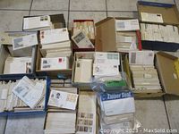 Open shoe boxes arranged on floor, filled with first day covers in sleeves and loose stacks.
