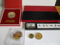 Large gold-tone 2008 Beijing Olympic mascots medallion in red presentation case with Olympic logos and text. Alongside Expo 2010 Shanghai gold-tone coin and stamps in separate case. Also shown are smaller Year of the Horse medallion and dragon coin in capsules for size comparison.