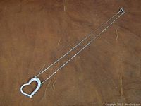 Full view of sterling silver chain with offset heart shaped pendant displayed flat on brown background.