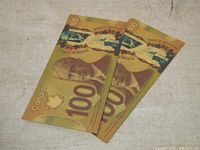 Two Canadian $100 bills laid overlapping, showing primarily front face with gold plating.