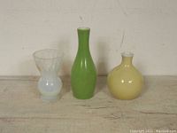 Front view of all three mini glass vases on a wood surface with a plain background
