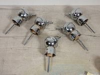 Five vintage bottle top jiggers laid out on a wooden surface, showing their rounded tops, spouts, and attachment ends.