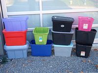 Full view of all 11 storage bins stacked outdoors showing variety of sizes and colors including purple, red, black, pink, green, blue and gray bins.