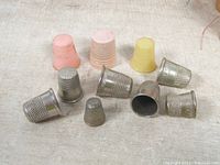 Top down view of the 10 vintage sewing thimbles arranged laying on fabric surface. Mixture of metal and plastic thimbles in various sizes shown.