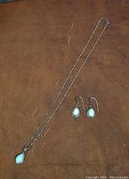 Photo showing the full necklace and earrings laid flat on a brown textured surface, clearly showing the teardrop shaped turquoise stones and silver settings.