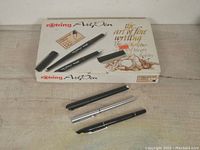 Three Rotring Art Pens placed with caps removed lying next to original box with artistic text and drawings visible