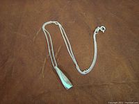 Full view of the silver chain and pendant on a brown surface showing the chain length and pendant design.