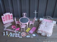 Full set of vintage pink and white doll furniture and accessories arranged outside on wooden floor.