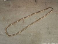 Full view of the 26-inch pearl necklace laid out flat on a light surface showing the entire length and uniform pearl size.