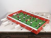 View of vintage Arcoflac tabletop foosball soccer game on wooden surface showing plastic player figures and metal rods with wooden handles.
