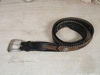 Photo showing the coiled black and brown leather belt with metal studs and woven pattern.