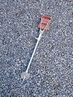 Full view of vintage gamebird shooting stick lying on gravel, showing metal shaft with leather seat folded up at top.