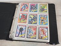 Open binder showing three rows of Marvel trading cards including Captain America, Daredevil, Professor X, Cyclops, and Iron Man.