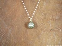 Front view of the vintage sterling silver basketball-shaped pendant on a chain, showing its spherical shape and basketball line engravings.