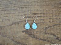 Full view of the turquoise earrings laid flat on wooden surface showing front of both earrings