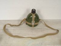 Front view of the olive green metal military canteen with full canvas shoulder strap attached and metal buckle.