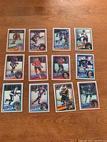 Top side of 12 OPC hockey cards from 1984-85 arranged on wood surface, showing player photos and names.