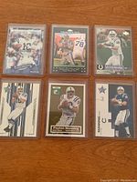 Six Peyton Manning football cards in protective plastic sleeves laid on wooden surface.