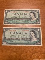Front side of two Canadian one dollar bills from 1954, showing Queen Elizabeth II portraits and serial numbers.