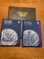 Photo showing three coin album books: Large Cents 1858-1920, Canada Dollars, and Canada 50 Cents, all appear empty.