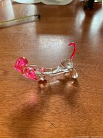 Side view of clear glass dog figurine showing pink ears and curved pink tail on wooden surface.