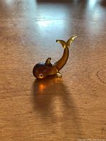 Side view of small amber glass whale figurine on wooden surface showing the curved upward tail and small dorsal fin.