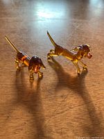 Two amber-colored glass dog figurines placed on a wooden surface, one standing with an open mouth, the other with a lowered head.