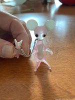 Close-up image of larger and smaller pink glass animal figurines connected by chain on wood surface.