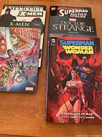 Top view of 5 graphic novels stacked showing Marvel and DC superhero cover art