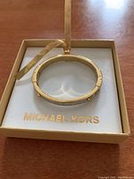 Gold-tone Michael Kors bangle bracelet resting inside a Michael Kors branded box with a gold-tone ribbon.