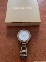Watch displayed on wooden surface with Michael Kors box behind