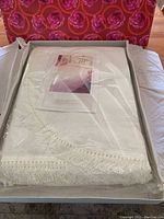 Sealed white bedspread folded inside plastic sleeve within original box, showing fringe detail on edge.
