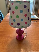 Front view of pink table lamp with white polka dot shade sitting on wooden table