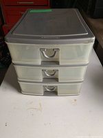 Front view of closed three-drawer plastic storage unit with gray top and handles