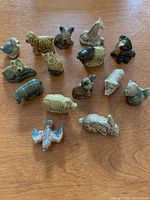 Top-down photo showing all 15 ceramic animal figurines arranged on a wooden surface, displaying their size and painted detail.