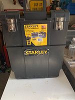Front view of Stanley toolbox showing the upper and lower compartments, Stanley logo, metal latches, and label with product info.