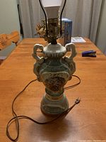 Full view of vintage porcelain table lamp with ornate double handles and painted scene.