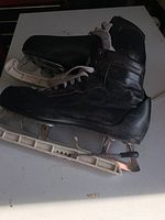 Side view of black leather goalie skate showing the full skate with white plastic holder and steel blade on a white surface.