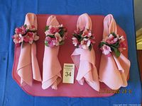 Four pink cloth napkins each wrapped with a plastic floral napkin ring featuring pink flowers and green leaves.