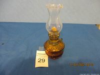 Full view of the amber glass oil lamp sitting on blue cloth background with a lamp height of 6.75 inches.