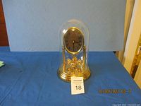 Full view of the gold-colored anniversary clock under glass dome, showing base, clock face, and rotary pendulum.